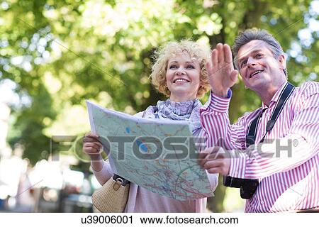 Stock Image - Happy middle-aged couple holding map in city. Fotosearch