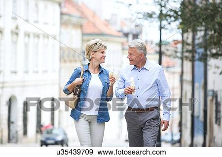 Happy middle-aged couple looking at each other while holding ice cream cones in city View Large Photo Image Stock Photo - Happy middle-aged couple looking at each other while holding ice cream cones in city. Fotosearch