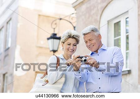 Happy middle-aged couple looking at pictures on digital camera in city View Large Photo Image Stock Photograph - Happy middle-aged couple looking at pictures on digital camera in city. Fotosearch