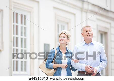Happy middle-aged couple standing with arm in arm outside building View Large Photo Image Stock Image - Happy middle-aged couple standing with arm in arm outside building. Fotosearch
