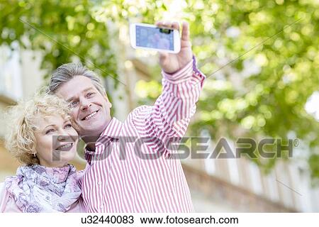 Happy middle-aged couple taking selfie through mobile phone outdoors View Large Photo Image Stock Image - Happy middle-aged couple taking selfie through mobile phone outdoors. Fotosearch