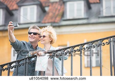 Happy middle-aged couple taking selfie against building View Large Photo Image Stock Photo - Happy middle-aged couple taking selfie against building. Fotosearch