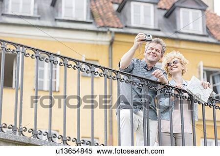Happy middle-aged couple taking selfie through digital camera against building View Large Photo Image Stock Photography - Happy middle-aged couple taking selfie through digital camera against building. Fotosearch