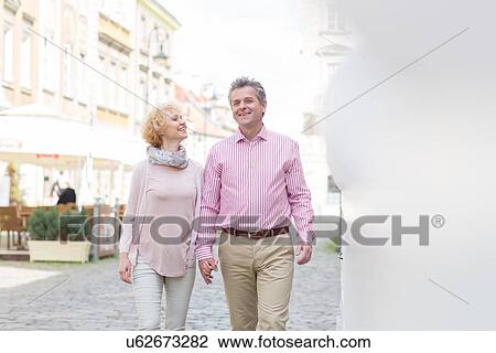 Happy middle-aged couple talking while walking in city View Large Photo Image Stock Image - Happy middle-aged couple talking while walking in city. Fotosearch