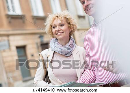Stock Image - Happy middle-aged couple with map in city. Fotosearch
