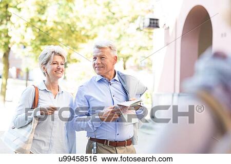 Stock Photograph - Happy middle-aged couple with map walking in city. Fotosearch