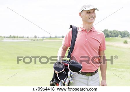Stock Photo - Happy middle-aged man looking away while carrying golf bag. Fotosearch