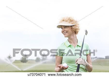 Happy middle-aged woman looking away while holding golf club and ball View Large Photo Image Stock Image - Happy middle-aged woman looking away while holding golf club and ball. Fotosearch