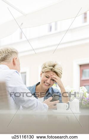 Happy middle-aged woman using mobile phone with man at sidewalk cafe View Large Photo Image Stock Image - Happy middle-aged woman using mobile phone with man at sidewalk cafe. Fotosearch