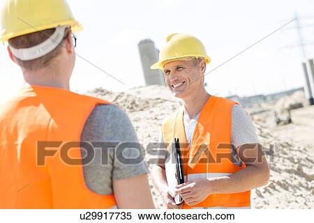 Stock Photography - Happy supervisor discussing with colleague at construction site. Fotosearch