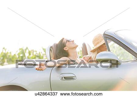 Stock Photo - Happy woman enjoying road trip in convertible with friend. Fotosearch