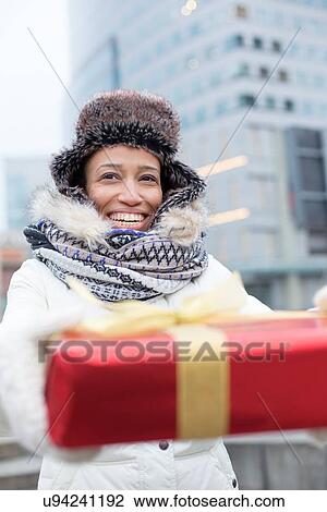Stock Image - Happy woman holding gift during winter in city. Fotosearch