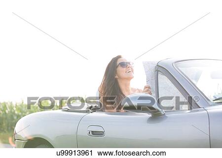 Happy woman holding map while sitting in convertible against clear sky View Large Photo Image Stock Image - Happy woman holding map while sitting in convertible against clear sky. Fotosearch