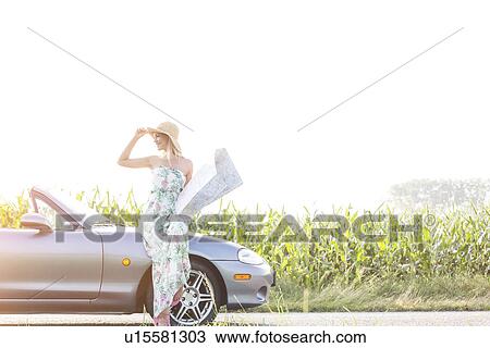 Happy woman holding map while standing by convertible on sunny day View Large Photo Image Stock Image - Happy woman holding map while standing by convertible on sunny day. Fotosearch