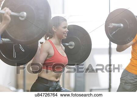 Picture - Happy woman lifting barbell in crossfit gym. Fotosearch
