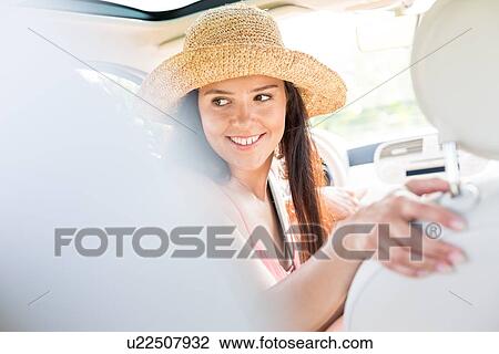 Happy woman looking back while driving car View Large Photo Image Stock Image - Happy woman looking back while driving car. Fotosearch