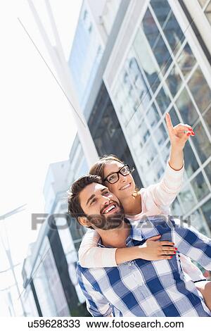 Happy woman showing something to man while enjoying piggyback ride in city View Large Photo Image Stock Image - Happy woman showing something to man while enjoying piggyback ride in city. Fotosearch