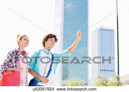 Picture - Happy woman standing with male friend hailing a taxi in city. Fotosearch