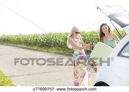 Happy women loading luggage in car trunk against clear sky View Large Photo Image Stock Photo - Happy women loading luggage in car trunk against clear sky. Fotosearch