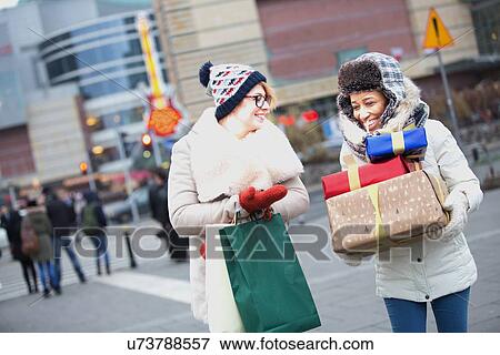 Happy women with gifts and shopping bags walking on city street during winter View Large Photo Image Stock Photo - Happy women with gifts and shopping bags walking on city street during winter. Fotosearch