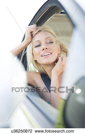 Stock Image - Happy young woman leaning on car window. Fotosearch