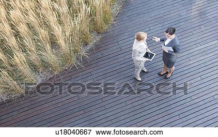 High angle view of businesswomen discussing while standing on floorboard View Large Photo Image Stock Photo - High angle view of businesswomen discussing while standing on floorboard. Fotosearch