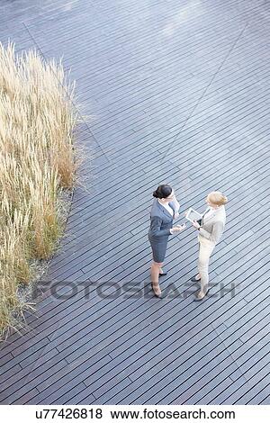 Stock Photo - High angle view of businesswomen discussing on floorboard. Fotosearch
