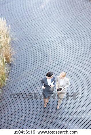 Stock Photograph - High angle view of businesswomen discussing while walking on floorboard. Fotosearch