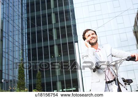 Low angle view of businessman answering mobile phone while sitting on bicycle outdoors View Large Photo Image Picture - Low angle view of businessman answering mobile phone while sitting on bicycle outdoors. Fotosearch