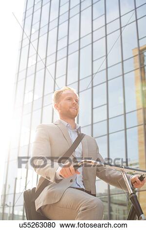 Low angle view of businessman riding bicycle outside office building on sunny day View Large Photo Image Stock Image - Low angle view of businessman riding bicycle outside office building on sunny day. Fotosearch