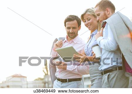 Stock Photo - Low angle view of businesspeople using digital tablet against clear sky. Fotosearch