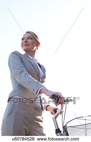 Stock Photo - Low angle view of businesswoman holding bicycle against clear sky. Fotosearch