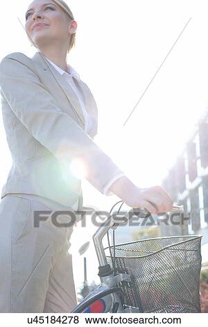 Low angle view of businesswoman standing with bicycle on sunny day View Large Photo Image Stock Photo - Low angle view of businesswoman standing with bicycle on sunny day. Fotosearch
