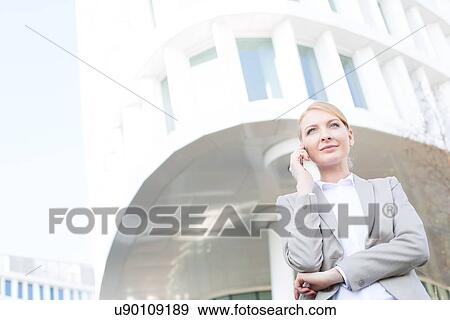 Stock Photo - Low angle view of businesswoman using cell phone outside office building. Fotosearch