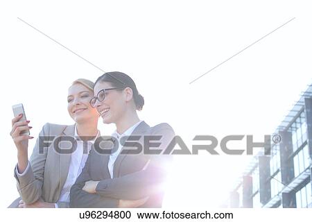 Low angle view of businesswomen using smart phone against clear sky on sunny day View Large Photo Image Stock Image - Low angle view of businesswomen using smart phone against clear sky on sunny day. Fotosearch