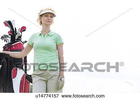 Stock Photo - Low angle view of confident female golfer standing against clear sky. Fotosearch