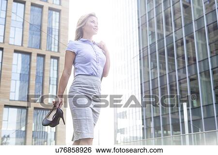 Low angle view of confident businesswoman holding high heels while standing outside office buildings View Large Photo Image Stock Photograph - Low angle view of confident businesswoman holding high heels while standing outside office buildings. Fotosearch