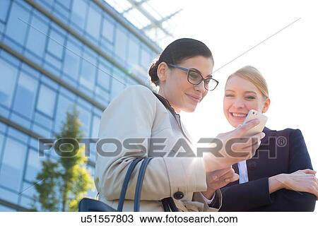 Low angle view of happy businesswomen using smart phone View Large Photo Image Stock Image - Low angle view of happy businesswomen using smart phone. Fotosearch