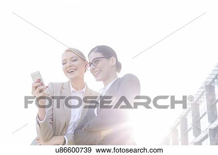 Low angle view of happy businesswomen using smart phone against clear sky on sunny day View Large Photo Image Stock Photo - Low angle view of happy businesswomen using smart phone against clear sky on sunny day. Fotosearch