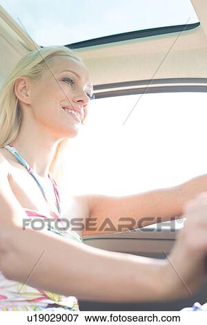 Stock Photo - Low angle view of happy woman driving car. Fotosearch