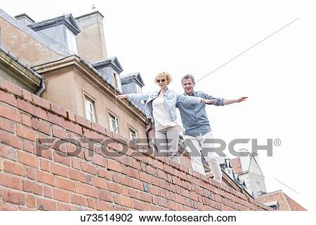 Low angle view of middle-aged couple with arms outstretched walking on brick wall against clear sky View Large Photo Image Stock Image - Low angle view of middle-aged couple with arms outstretched walking on brick wall against clear sky. Fotosearch