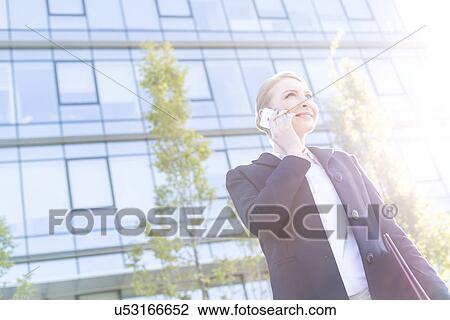 Low angle view of smiling businesswoman using cell phone on sunny day View Large Photo Image Stock Image - Low angle view of smiling businesswoman using cell phone on sunny day. Fotosearch