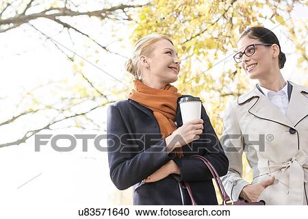 Low angle view of smiling businesswomen conversing at park View Large Photo Image Stock Image - Low angle view of smiling businesswomen conversing at park. Fotosearch
