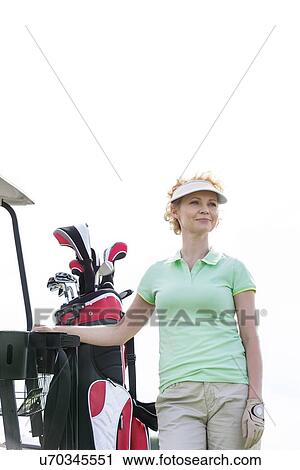 Stock Image - Low angle view of smiling golfer standing against clear sky. Fotosearch