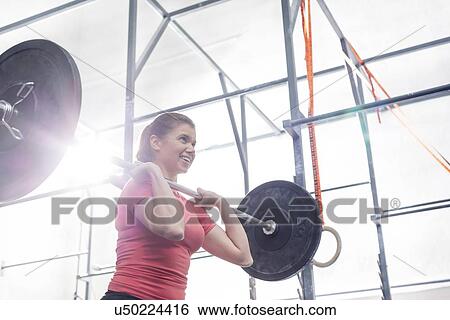 Stock Photograph - Low angle view of smiling woman lifting barbell in crossfit gym. Fotosearch
