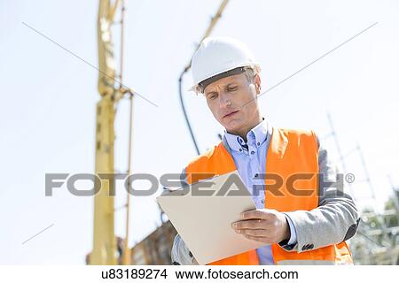 Picture - Low angle view of supervisor writing on clipboard at construction site. Fotosearch