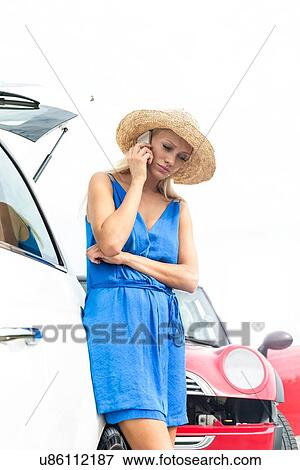 Stock Photo - Low angle view of tensed woman using cell phone by broken down cars. Fotosearch