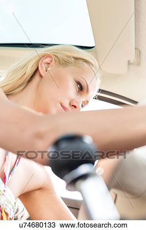 Stock Image - Low angle view of woman sitting in car. Fotosearch