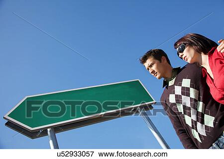 Stock Photo - Low angle view of young couple with arm around. Fotosearch