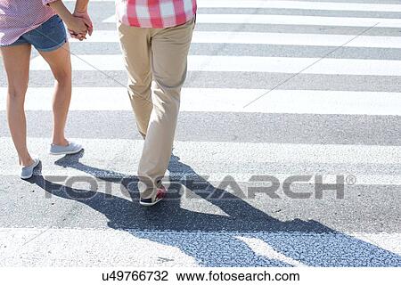 Stock Image - Low section of couple walking on crosswalk. Fotosearch